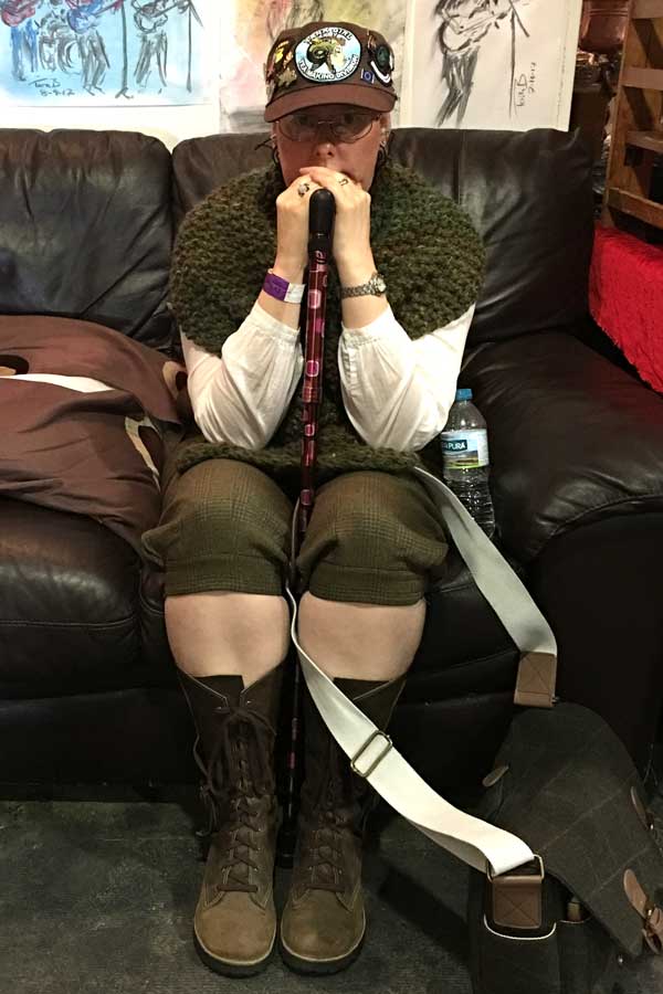 Claire sitting on a comfy sofa, leaning on her walking stick. She is wearing a comfortable steampunk costume.