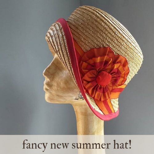 A straw cloche hat with orange and red ribbons made into the shape of a pansy. Made by Mind Your Bonce Millinery