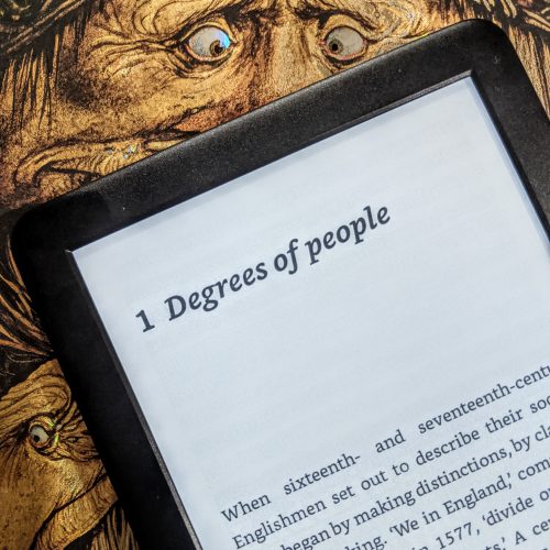 An image of a Kindle, sitting on top of a book cover with illustrations by Brian Froud